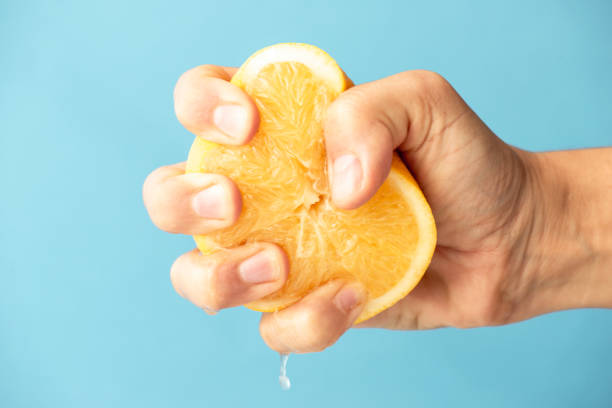 A hand squeezing an orange that has been cut in half.