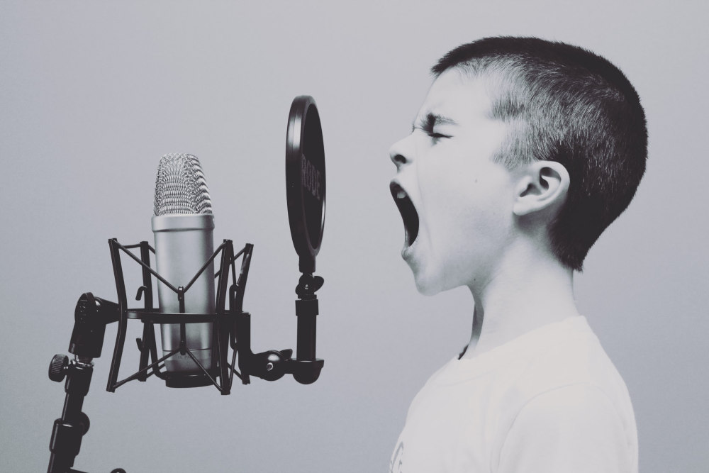 A young boy passionately screaming or singing into a studio microphone.